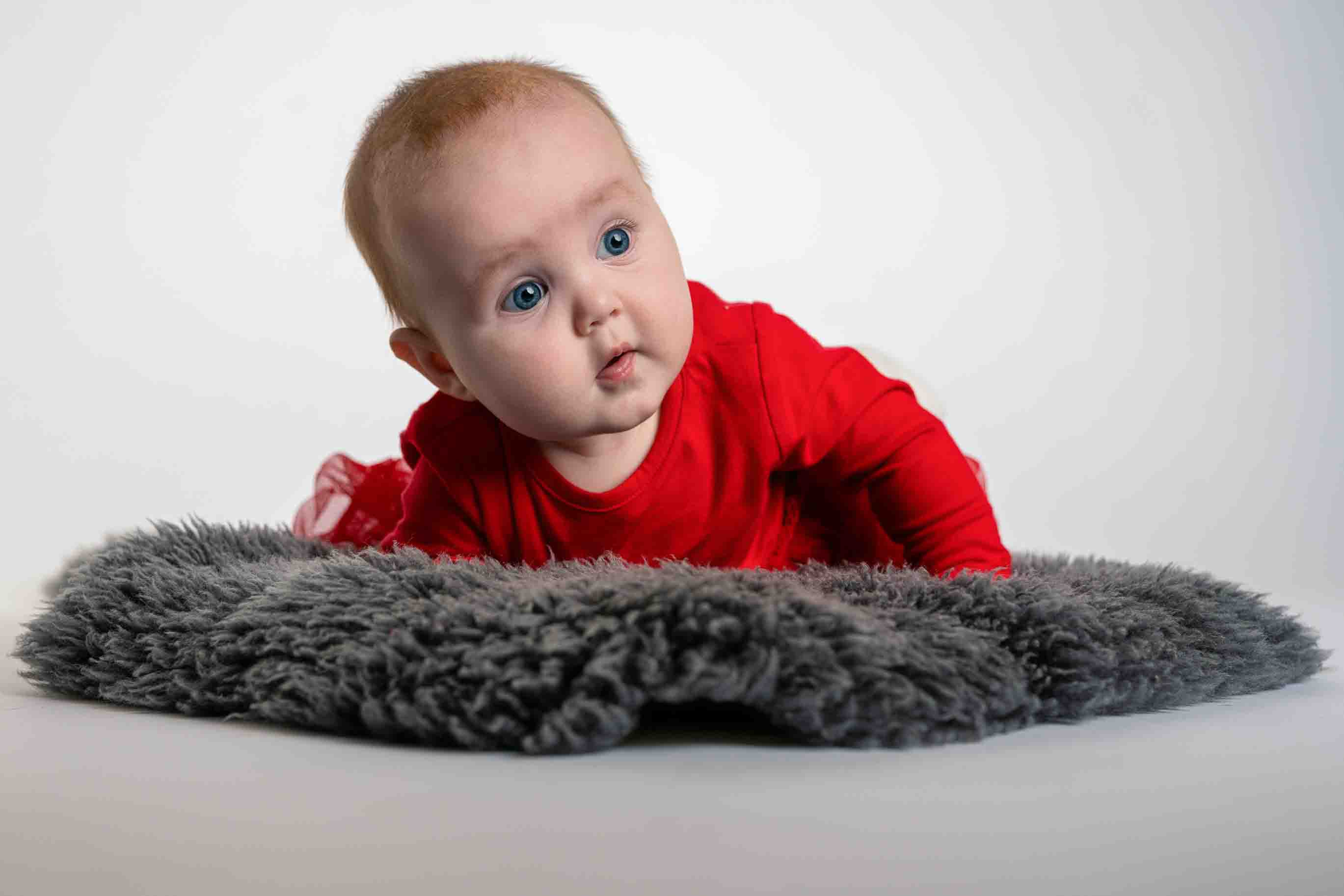 Baby i röd tröja fotograferad mot ljus bakgrund