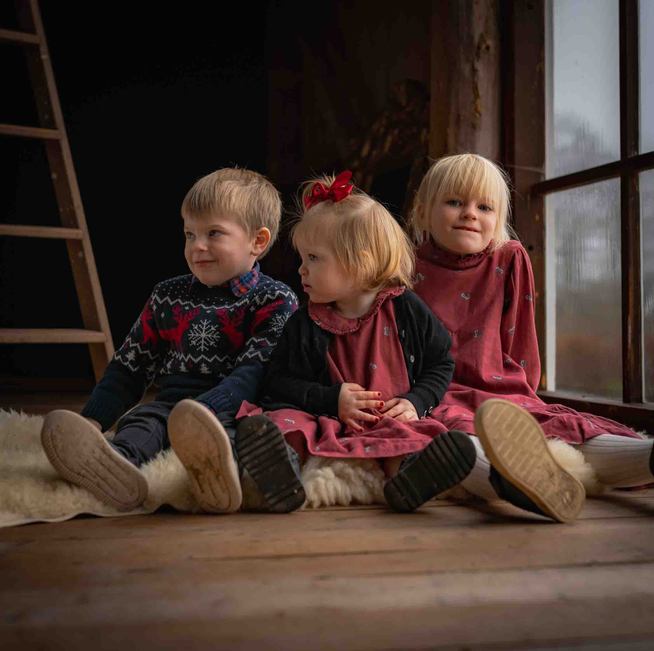 Tre syskon fotograferade tillsammans vid ett stort fönster